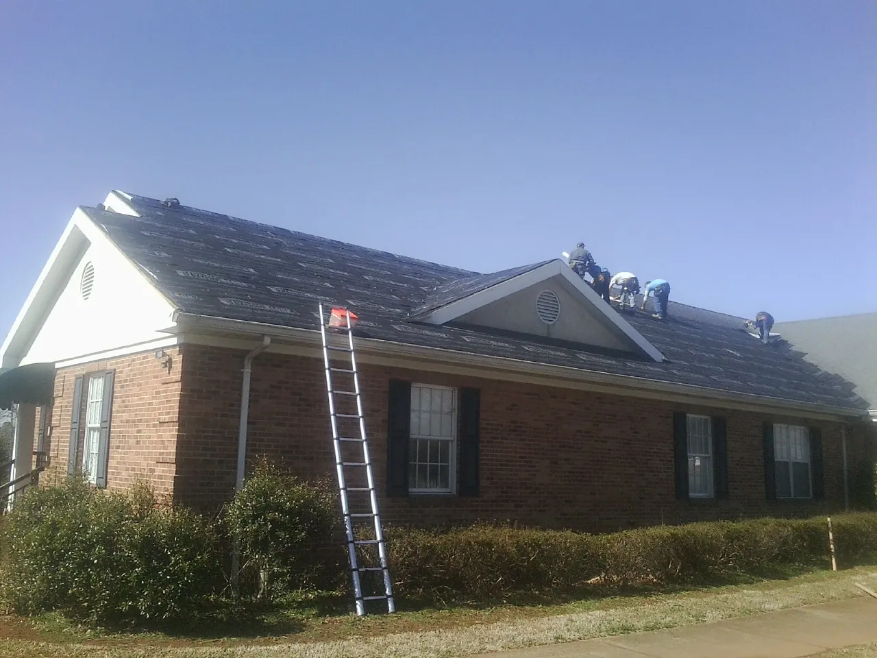 Crew tearing shingles off a brick ranch roof with a ladder set — Emergency Roof Repair work by our crew in Forest Knolls