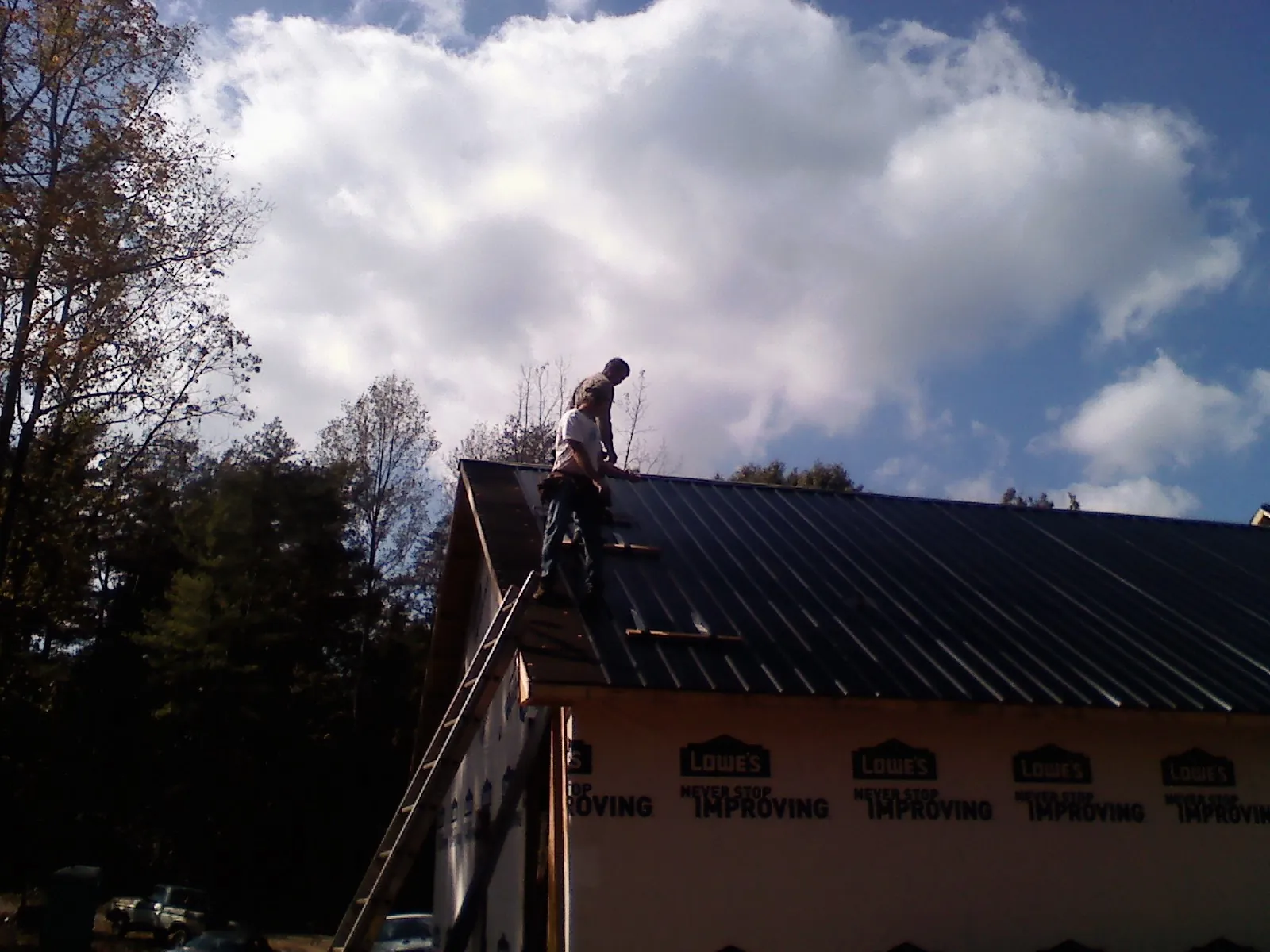 Roofer fastening dark metal panels high against a cloudy sky, from a Roof Inspection job in Forest Knolls