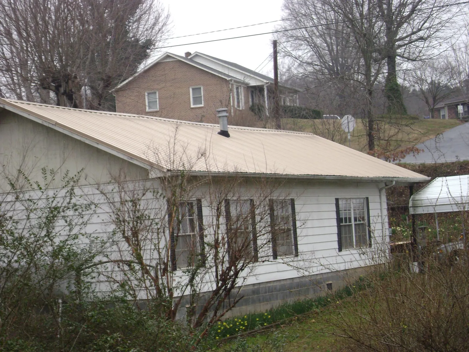 Tan metal roof on a white sided house set into a hillside — Commercial Roofing by Roofing Brothers in Forest Knolls
